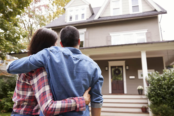 young couple standing outside their first home buyers